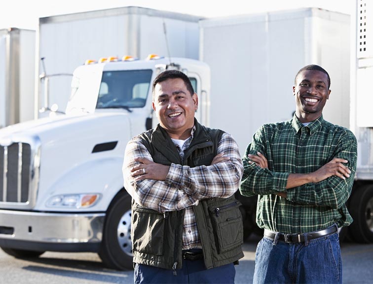 Image of two men smiling with their arms crossed standing in front of white trucks