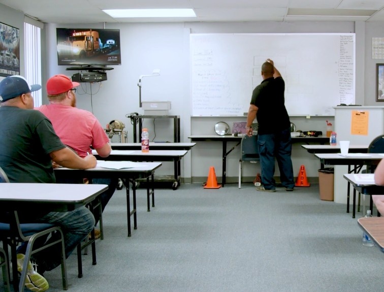 Instructor writing on whiteboard in a classroom with students sitting at desks