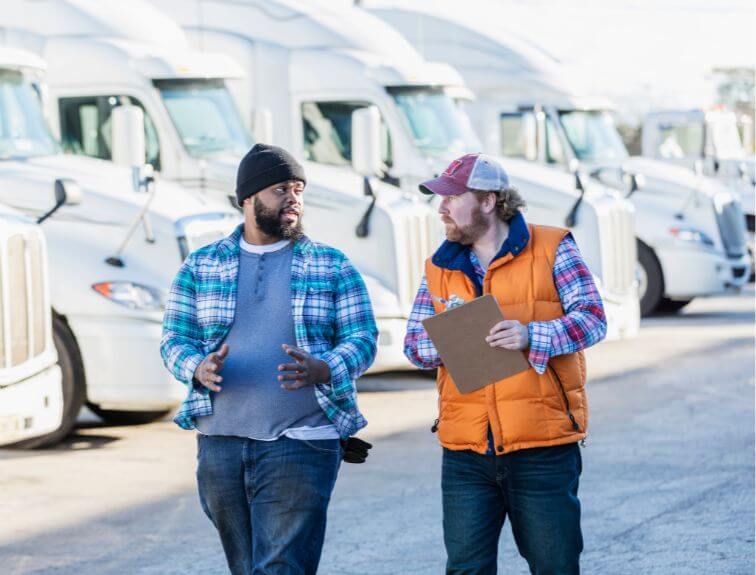image of two truck drivers talking in front of a row of white semi trucks