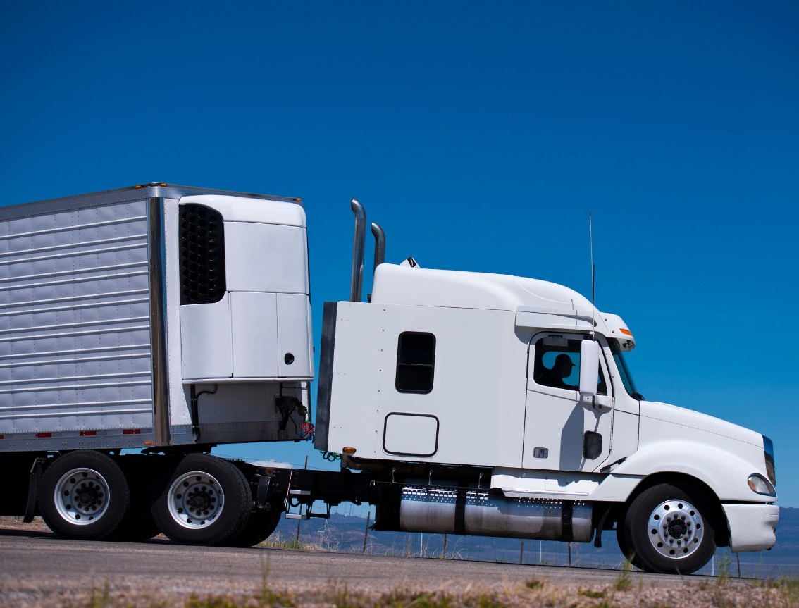 White refrigerated reefer semi-truck on a desert highway under a clear blue sky