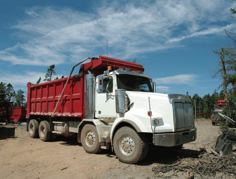 Image of a red and white dump truck on sand with a blue sky.