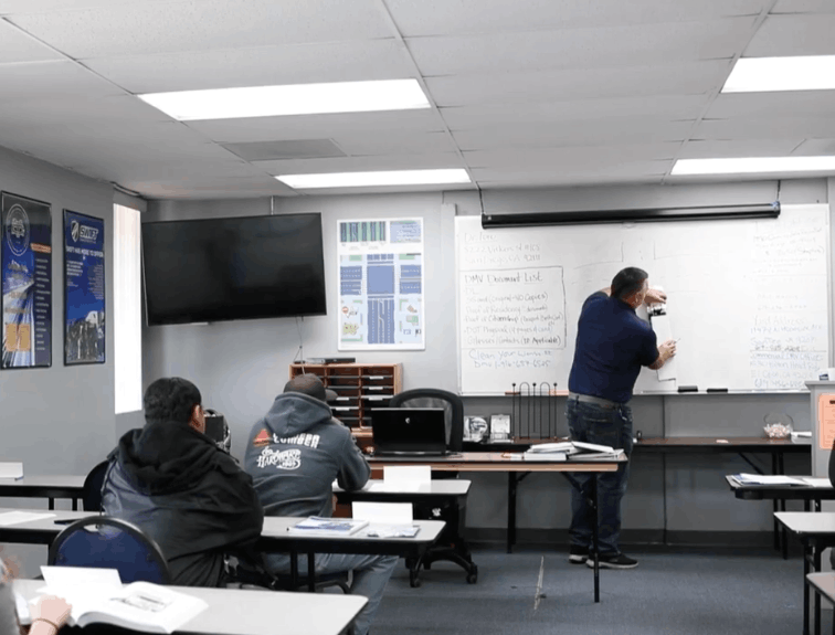 Instructor drawing on white board, students at classroom desks