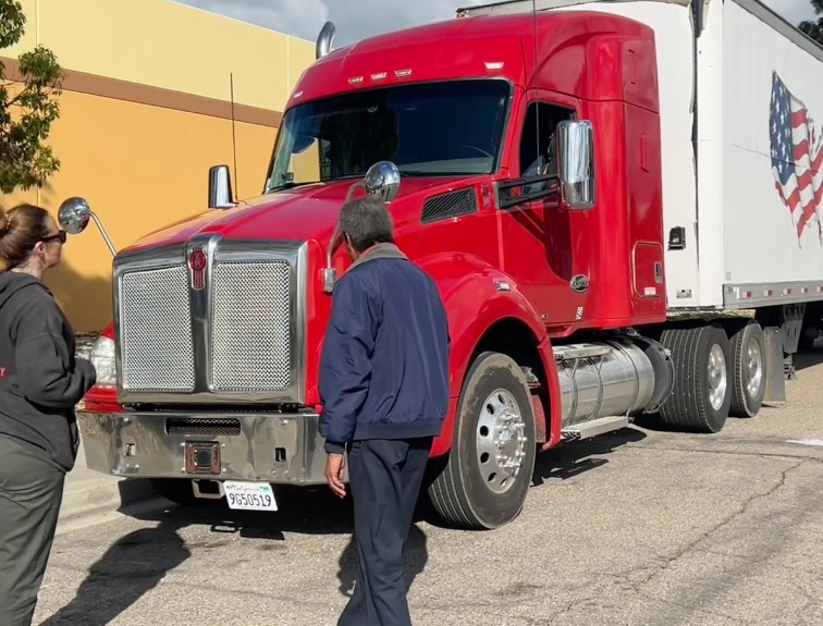 Two CDL students walk toward a red semi-truck with an American flag trailer wrap during hands-on truck driver training