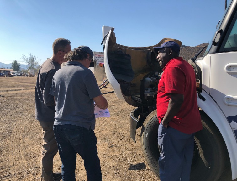 Instructor pointing to inside engine of semi truck with students watching